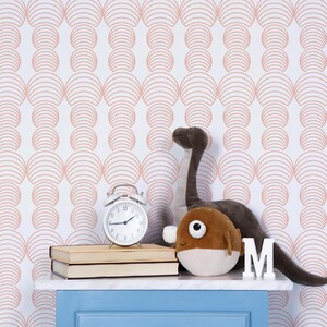 May include: A white wall with a pink geometric pattern wallpaper. A blue nightstand with two books and a white alarm clock. A brown plush pufferfish and a brown dinosaur plush toy are on the nightstand. The letter "M" is on the nightstand.