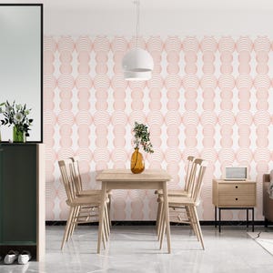May include: A dining room with a white wall featuring a pink geometric pattern wallpaper. A wooden table with four chairs is in the center of the room. A white pendant light hangs above the table.