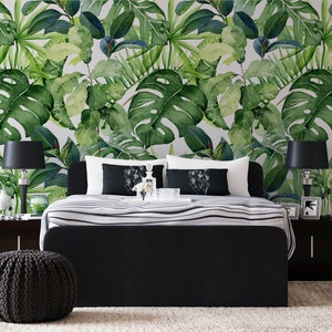Op de afbeelding: Een zwart bedframe met een wit en zwart gestreept beddengoed. Het hoofdeinde staat tegen een muur met een tropische bladbehang. Twee zwarte lampen met witte lampenkappen staan aan weerszijden van het bed.