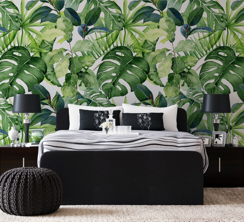 Op de afbeelding: Een zwart bedframe met een wit en zwart gestreept beddengoed. Het hoofdeinde staat tegen een muur met een tropische bladbehang. Twee zwarte lampen met witte lampenkappen staan aan weerszijden van het bed.