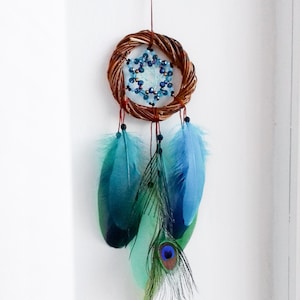 May include: A blue and green dreamcatcher with a brown wooden hoop and beaded centre. The dreamcatcher has three feathers, two blue and one green with a peacock eye.