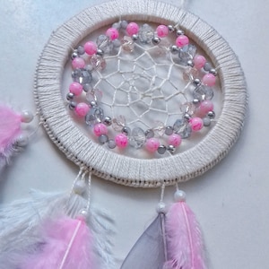 May include: A white dream catcher with pink and silver beads, and white, pink, and grey feathers.