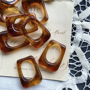 May include: A group of amber-coloured plastic rings, some with a square shape and some with a rounded shape. The rings are arranged on a piece of paper with handwritten text.