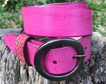 May include: A pink leather belt with a silver oval buckle. The belt is distressed and has a floral pattern on the underside.