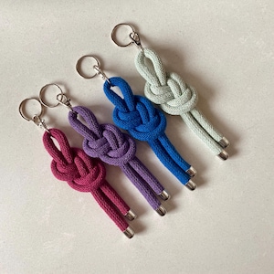 May include: Four keychains with different coloured rope knots. The keychains are made of a soft, woven rope and feature a simple knot design. The colours are green, blue, purple, and red.