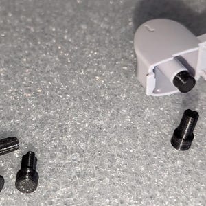 May include: A close-up of a white plastic part with a black screw. There are nine black screws scattered around the part.