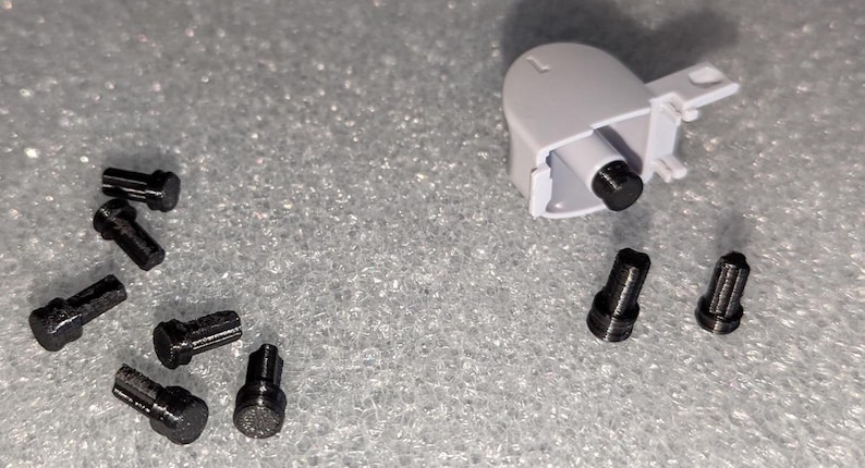 May include: A close-up of a white plastic part with a black screw. There are nine black screws scattered around the part.