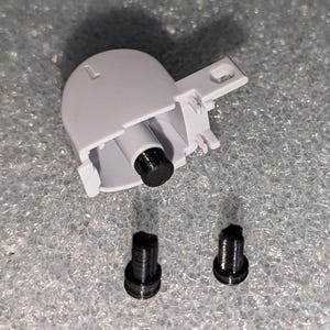 Könnte beinhalten: Ein weißes Kunststoffteil mit einer schwarzen Schraube und zwei schwarzen Schrauben auf einer grauen Oberfläche.