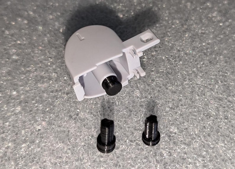May include: A white plastic part with a black screw and two black screws on a gray surface.