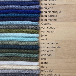 May include: A stack of knitted fabric swatches in various colors, including shades of blue, green, white, cream, gray, and black. Each swatch is labeled with French text identifying the color, such as bleu glacier, vert sauge, and noir.