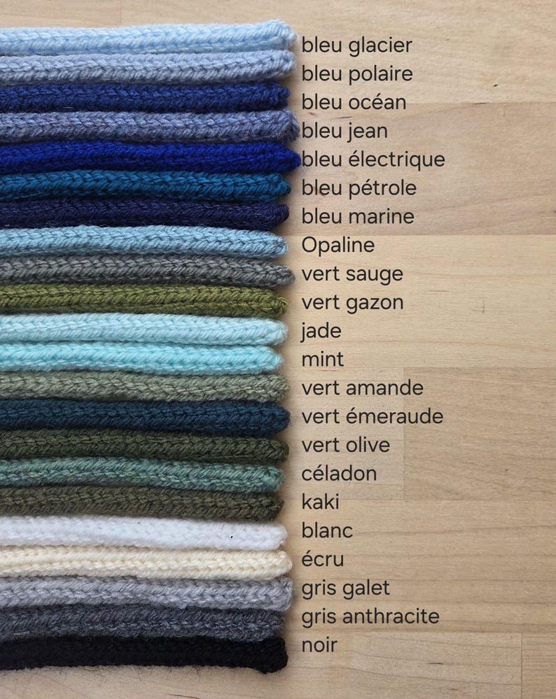 May include: A stack of knitted fabric swatches in various colors, including shades of blue, green, white, cream, gray, and black. Each swatch is labeled with French text identifying the color, such as bleu glacier, vert sauge, and noir.
