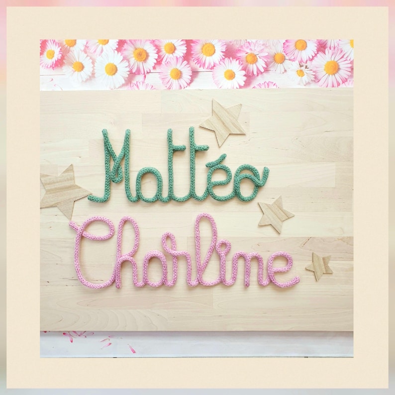May include: A light wood board featuring the names Matteo in green yarn and Charline in pink yarn, written in a cursive script. The board is decorated with four light wood star cutouts and a border of white and yellow daisy flowers.