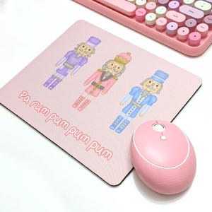 May include: A pink mousepad with three illustrated nutcracker figures in different colors. The text "Pa rum pum pum pum pum" is printed on the mousepad.