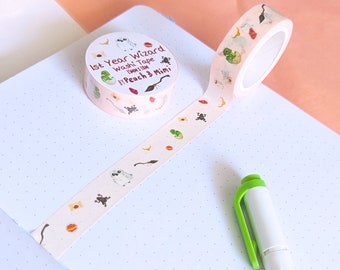 Könnte beinhalten: Eine rosa und weiße Washi-Tape-Rolle mit einem verspielten Design mit Eulen, Fröschen und anderen magischen Kreaturen. Das Band ist mit "1st Year Wizard Washi Tape 1mm/11m by Peach & Mimi" beschriftet.