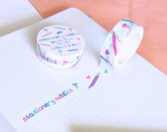 May include: Two rolls of washi tape with a white background and colorful illustrations of pencils, hearts, and paper clips. The tape is labeled "stationery addict. Washi Tape 110M by Peach & Mimi".