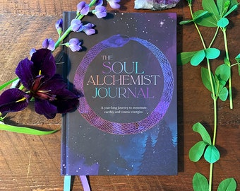 May include: A dark purple journal with a silver snake design and the text "THE SOUL ALCHEMIST JOURNAL. A year-long journey to transmute earthly and cosmic energies".
