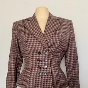 May include: A vintage brown and burgundy plaid blazer with a double-breasted button closure. The blazer features a fitted waist and long sleeves with folded cuffs. The garment is displayed on a mannequin.