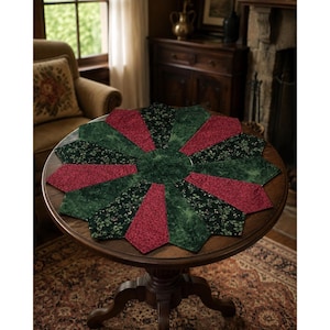 May include: A circular fabric table topper featuring a starburst pattern of alternating segments. The segments consist of dark green fabric with a subtle mottled texture and deep red fabric with a small-scale floral print, centered by a green circle.