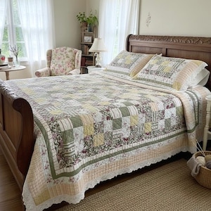 May include: A patchwork quilt with a floral and geometric pattern in shades of green, yellow, and cream covers a wooden bed. The quilt has a scalloped lace edge. Two matching pillow shams are on the bed.