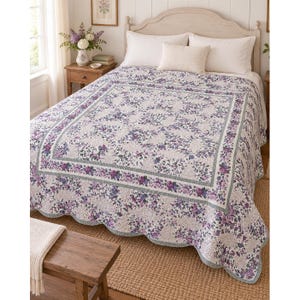 May include: A bedspread featuring a white background with a dense pattern of purple and blue floral clusters. The quilt has a wide border with a repeating floral design and a scalloped edge, paired with two white pillows and a textured throw.