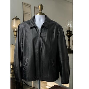 May include: A black leather jacket with a collared neckline and a full-length zipper closure. The jacket has two front pockets and is displayed on a mannequin. The jacket is a classic style.