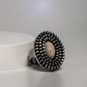 Puede incluir: Un anillo de plata con una piedra ovalada texturizada blanca rodeada de un diseño circular de púas de plata.