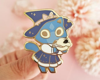 May include: A blue and gold enamel pin of a cartoon wolf wearing a witch's hat and holding a bone. The wolf is wearing a blue and white dress with stars and a white collar.
