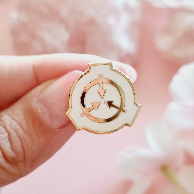 May include: A white enamel pin with a gold outline featuring the logo of the fictional organization, the SCP Foundation. The logo is a white circle with three arrows pointing inwards, surrounded by a white, geometric shape.