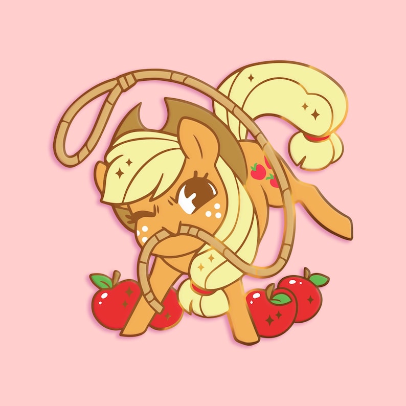 K&ouml;nnte beinhalten: Eine goldfarbene Emaille-Anstecknadel mit einem Cartoon-Pony mit gelber M&auml;hne und Schwanz, das einen Cowboyhut tr&auml;gt und ein Lasso h&auml;lt. Das Pony ist von roten &Auml;pfeln umgeben.