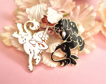 May include: Two enamel pins featuring stylized unicorn figures with gold-toned metal outlines. One pin is white with gold star accents, and the other is black with gold star accents. Both unicorns are depicted in a dynamic, leaping pose.
