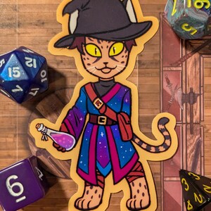 May include: A sticker of a cartoon cat wearing a wizard hat and robe. The cat is holding a potion bottle and has a starry sky pattern on its robe. The sticker is on a wooden background with dice.
