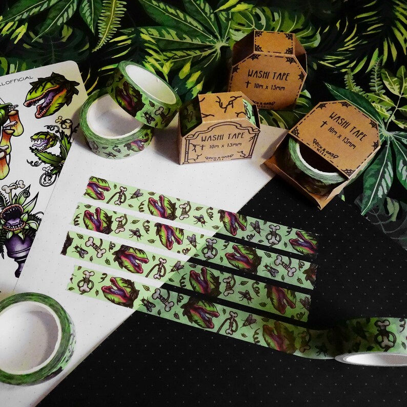 Op de afbeelding: Assortiment van groene en zwarte washi tape rollen met een vleesetend plantenontwerp. De tape is 10 meter lang en 13 millimeter breed. De tape is verpakt in een bruine kartonnen doos met de tekst "Washi Tape" erop gedrukt.
