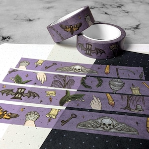 Op de afbeelding: Paarse washi tape met verschillende griezelige ontwerpen, waaronder een schedel met vleugels, een vleermuis, een hand, een sleutel, een kaars, een wilg, een nachtvlinder en een halve maan.