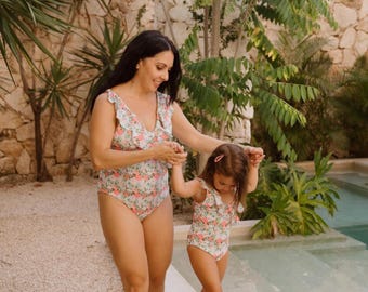 Peut inclure: Deux maillots de bain une pièce avec une base blanche et un motif floral aux tons roses, verts et bleus. Chaque maillot présente un décolleté en V profond, des volants sur les épaules et une échancrure haute au niveau des jambes.