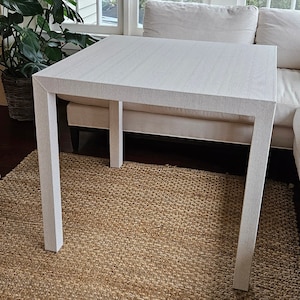 May include: White rectangular table with a woven top and four legs. The table is sitting on a woven rug.