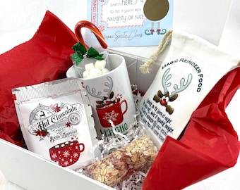 May include: A white gift box filled with Christmas themed items, including a mug with a reindeer design, a packet of hot chocolate mix, a bag of reindeer food, and a candy cane. The box also includes a card with a scratch-off area to reveal if someone has been naughty or nice.