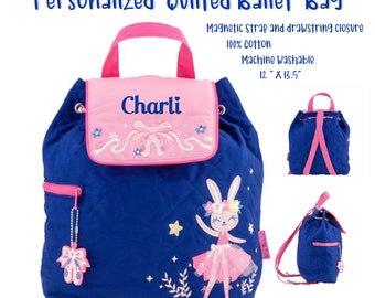 May include: A blue quilted ballet bag with a pink flap and a drawstring closure. The bag features a ballerina bunny design and the name "Charli" embroidered on the flap. The bag is 12 inches by 13.5 inches.