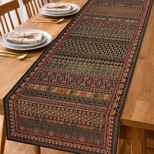 Puede incluir: Un camino de mesa rectangular con un intrincado patrón de formas geométricas y motivos florales en tonos verdes, marrones y rojos. El camino de mesa está colocado sobre una mesa de madera, añadiendo un toque decorativo al comedor.