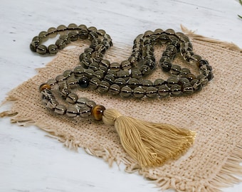 May include: A dark brown gemstone mala with a tassel. The mala is made of round beads and has a brown and gold tiger eye bead.