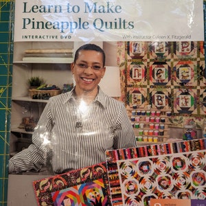 May include: A DVD cover for a quilting class titled "Learn to Make Pineapple Quilts". The cover features a smiling woman wearing a striped shirt and a colorful pineapple quilt. The text "Includes Book and Class DVD" is in a red box at the top of the cover. The text "Interactive DVD" is below the title. The text "With instructor Gyleen X. Fitzgerald" is at the bottom of the cover.