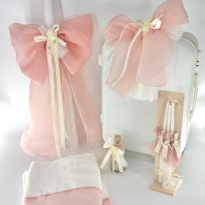 May include: A selection of baptism or wedding decorations in soft pink and white. The set includes candles, bows, a small bottle, towels, and a decorative candle holder, all adorned with ribbons and pearls.