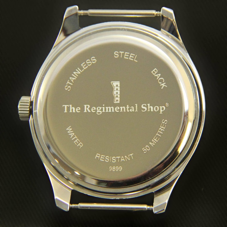 May include: A stainless steel watch back with the text "The Regimental Shop" and "Water Resistant 50 Metres". The watch has a silver-coloured metal casing and a crown on the side.