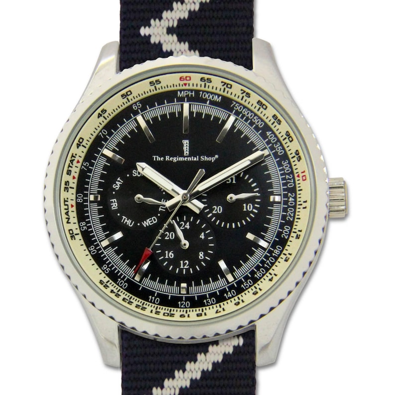 May include: A silver wristwatch with a black face and a navy blue and white striped strap. The watch face displays multiple sub-dials, including day and date indicators, and the text "The Regimental Shop". The watch has a rotating bezel with speed markings.