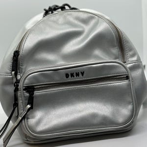 Mochila plateada DKNY con asa de cadena negra. 30 cm de largo x 28 cm de ancho x 7,6 cm de profundidad. Interior plateado.