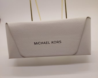 Étui à lunettes rigide Michael Kors. Extérieur en vinyle blanc. Feutre gris à l'intérieur. 6 po. L X 2 1/2 po. L X 1 1/2 po. P.