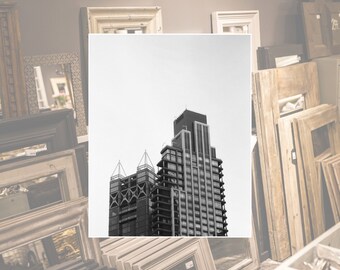 May include: A black and white photo of a modern skyscraper building against a white sky. The building is surrounded by wooden picture frames.