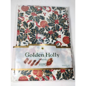 Puede incluir: Un mantel rectangular en un paquete de plástico con el texto Golden Holly Tablecloth Bardwil Linens y el tamaño 60 x 102 inches. La tela presenta un patrón de hojas de acebo verde oscuro, bayas rojas y adornos dorados sobre un fondo blanco.