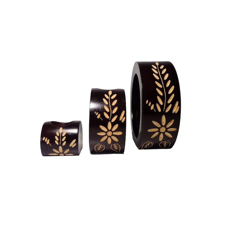 Peut inclure: Ensemble de trois bougeoirs en bois brun avec un motif floral. Les bougeoirs sont de tailles diff&eacute;rentes et sont dispos&eacute;s en rang&eacute;e du plus grand au plus petit.