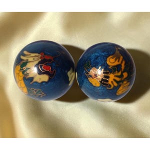 May include: Two blue decorative balls with intricate dragon designs in gold, yellow, and red. The balls have a glossy finish and are set against a soft, golden background. These decorative balls are likely used for stress relief or meditation.