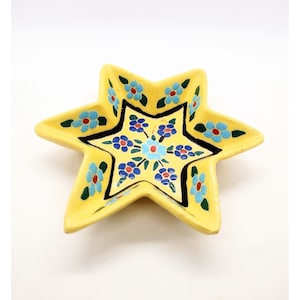 May include: A yellow ceramic star-shaped dish with a blue and green floral design. The dish is perfect for serving small snacks or holding jewelry.